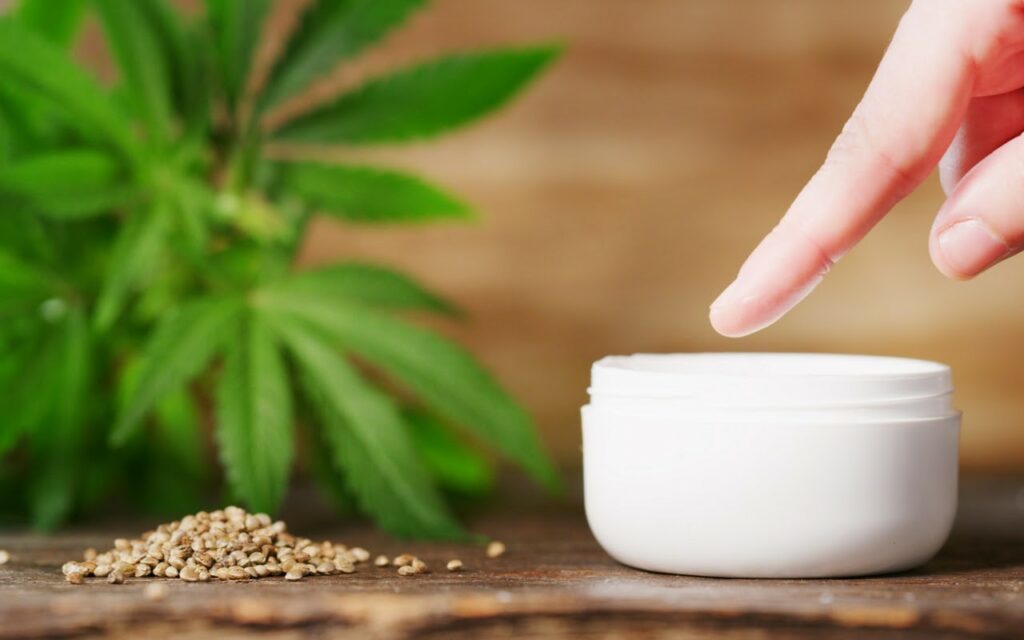 CBD Cream in White Pot with Cannabis Leaves in the Background
